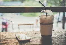 Cacao helado, chocolate, con crema del azote en taza plástica y teléfono móvil en la tabla de madera imágenes de archivo libres de regalías Cacao helado, chocolate, con crema del azote en taza plástica y teléfono móvil en la tabla de madera imágenes de archivo libres de regalías