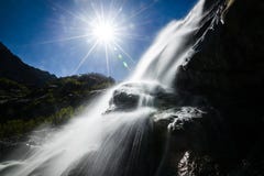Cachoeira nas montanhas, no lado, no luminoso, o sol no quadro, brilho do sol Dombay, cachoeira de Alibek imagens de stock Cachoeira nas montanhas, no lado, no luminoso, o sol no quadro, brilho do sol Dombay, cachoeira de Alibek imagens de stock