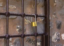 Cadeado na estrutura Grade antiga do metal em que um castelo dourado pesa contra uma parede de pedra foto de stock royalty free Cadeado na estrutura Grade antiga do metal em que um castelo dourado pesa contra uma parede de pedra foto de stock royalty free