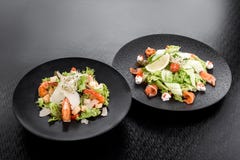 Caesar sallad med räkor och sallad med laxen, gräddost och gurkan på svarta plattor på en mörk bakgrund arkivbilder Caesar sallad med räkor och sallad med laxen, gräddost och gurkan på svarta plattor på en mörk bakgrund arkivbilder