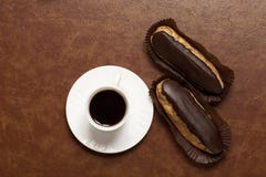 Caffè, Eclair di cioccolato, caffè in una tazza bianca, piattino bianco, su una tavola marrone, Eclair sul supporto della carta fotografie stock libere da diritti Caffè, Eclair di cioccolato, caffè in una tazza bianca, piattino bianco, su una tavola marrone, Eclair sul supporto della carta fotografie stock libere da diritti