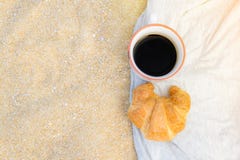 Café preto e croissant no fundo da areia, no café da manhã na praia, no alimento e no conceito da bebida foto de stock royalty free Café preto e croissant no fundo da areia, no café da manhã na praia, no alimento e no conceito da bebida foto de stock royalty free