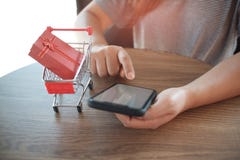 Caixa de presente vermelha no carrinho de compras com as mulheres que usam o telefone celular para o conceito de compra em linha foto de stock royalty free Caixa de presente vermelha no carrinho de compras com as mulheres que usam o telefone celular para o conceito de compra em linha foto de stock royalty free