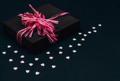 Caja de regalo negra con el arco rosado de la cinta en el fondo negro asperjado con confeti en forma de corazón Copie el espacio imagen de archivo libre de regalías Caja de regalo negra con el arco rosado de la cinta en el fondo negro asperjado con confeti en forma de corazón Copie el espacio imagen de archivo libre de regalías
