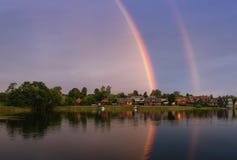 Calm summer landscape with double rainbow above the lake, blue sky and boats.