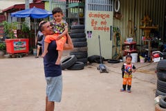 Man with a child in his arms near the tire shop, slums of Asia, residents of poor areas of the stock image Man with a child in his arms near the tire shop, slums of Asia, residents of poor areas of the stock image