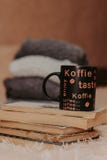 Camisetas de lã feitas malha de dobramento, uma pilha de livros velhos, um copo preto e vermelho bonito em uma cobertura bege mac imagens de stock royalty free Camisetas de lã feitas malha de dobramento, uma pilha de livros velhos, um copo preto e vermelho bonito em uma cobertura bege mac imagens de stock royalty free