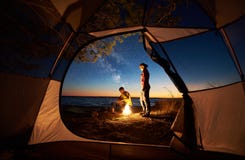 Young couple man and woman having rest at tourist tent and burning campfire on sea shore near forest royalty free stock image Young couple man and woman having rest at tourist tent and burning campfire on sea shore near forest royalty free stock image