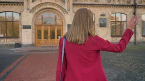 Cantidad del estudiante joven femenino joven que camina a la entrada de la universidad que agita con su mano, saludo, de la parte metrajes Cantidad del estudiante joven femenino joven que camina a la entrada de la universidad que agita con su mano, saludo, de la parte metrajes