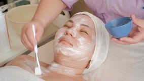 Cara de uma menina asiática em um salão de beleza O esteticista aplica um creme branco da massagem à área do pescoço de uma mulhe vídeos de arquivo Cara de uma menina asiática em um salão de beleza O esteticista aplica um creme branco da massagem à área do pescoço de uma mulhe vídeos de arquivo