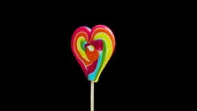 Caramel lollipop heart multicolored on a stick spinning on a black background. Candy cane spiral copy space.