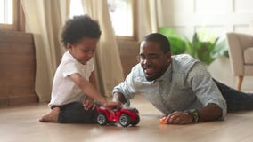 African father and little son playing with toy cars indoors