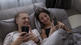 Casal novo que usa seu telefone celular ao encontrar-se na cama e ao compartilhar de imagens engraçadas do telefone entre si filme Casal novo que usa seu telefone celular ao encontrar-se na cama e ao compartilhar de imagens engraçadas do telefone entre si filme