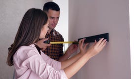 Casal positivo com fita métrica nas mãos que penduram a prateleira na parede após o reparo no apartamento video estoque Casal positivo com fita métrica nas mãos que penduram a prateleira na parede após o reparo no apartamento video estoque