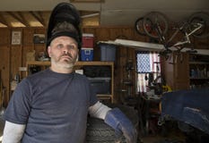 Casco de la soldadura del hombre que lleva que se inclina contra el neumático imagen de archivo Casco de la soldadura del hombre que lleva que se inclina contra el neumático imagen de archivo