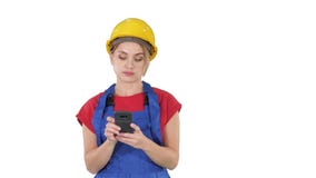 Casco que lleva del contratista femenino profesional joven que manda un SMS con el teléfono celular en el fondo blanco almacen de metraje de vídeo Casco que lleva del contratista femenino profesional joven que manda un SMS con el teléfono celular en el fondo blanco almacen de metraje de vídeo