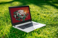 Casino en línea, ordenador portátil con el dispositivo de las fichas de póker sobre hierba verde juego imagen de archivo libre de regalías Casino en línea, ordenador portátil con el dispositivo de las fichas de póker sobre hierba verde juego imagen de archivo libre de regalías
