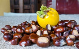 Castagne su una tovaglia rustica, fuori, con un cachi giallo fotografia stock Castagne su una tovaglia rustica, fuori, con un cachi giallo fotografia stock