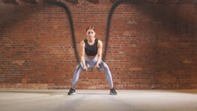 Caucasian fit woman exercising with battle ropes at gym. stock footage Caucasian fit woman exercising with battle ropes at gym. stock footage