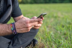 Caucasian male texting on cell, sitting on grass outside with rainbow bracelets stock photo Caucasian male texting on cell, sitting on grass outside with rainbow bracelets stock photo