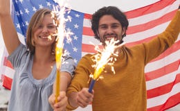 Caucasian par som spelar med brandsmällaren, medan rymma amerikanska flaggan royaltyfri fotografi Caucasian par som spelar med brandsmällaren, medan rymma amerikanska flaggan royaltyfri fotografi