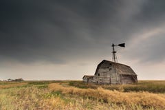 Celeiro, escaninhos e moinho de vento do vintage sob céus escuros sinistros em Saskatchewan, Canadá imagem de stock Celeiro, escaninhos e moinho de vento do vintage sob céus escuros sinistros em Saskatchewan, Canadá imagem de stock