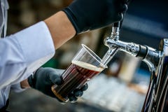 Cerveja escura de derramamento ao vidro plástico da torneira da cerveja imagem de stock Cerveja escura de derramamento ao vidro plástico da torneira da cerveja imagem de stock