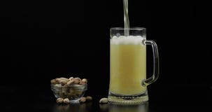 A cerveja est? derramando no vidro no fundo preto Bacia de porcas de pistaches imagem de stock A cerveja est? derramando no vidro no fundo preto Bacia de porcas de pistaches imagem de stock