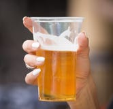 Cerveja fresca em um copo plástico na mão fotografia de stock Cerveja fresca em um copo plástico na mão fotografia de stock