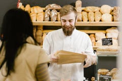 Charismatic baker with a beard and mustache gives a paper bag of bread to the customer in the bakery stock photography Charismatic baker with a beard and mustache gives a paper bag of bread to the customer in the bakery stock photography