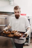 Charismatic baker holds the baking tray with newly-baked bread in the bakery stock image Charismatic baker holds the baking tray with newly-baked bread in the bakery stock image