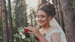 Charmante en gelukkige bruid in een mooie huwelijkskleding met een boeket van bloemen in een pijnboombos in de zon De dag van het stock videobeelden Charmante en gelukkige bruid in een mooie huwelijkskleding met een boeket van bloemen in een pijnboombos in de zon De dag van het stock videobeelden