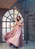 Charming tender princess in long peach pink shiny satin flying waving dress with neckline, girl stands on vintage stairs stock image Charming tender princess in long peach pink shiny satin flying waving dress with neckline, girl stands on vintage stairs stock image