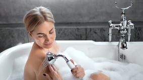 Charming young sexy woman taking shower enjoying bathing surrounded by foam medium shot