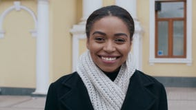 Cheerful african american lady in warm coat and scarf smiling to camera outdoor, tracking shot