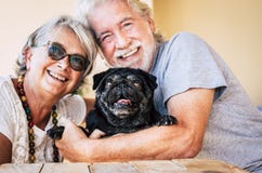 Cheerful Alternative Family With Old Senior Couple People And Funny Black Pug Dog Hug Together In Love Activity - Portrait Of Stock Photos