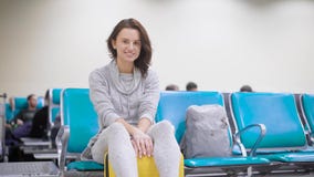 Cheerful brunette girl is sitting on bag in airport and waiting her flight, enjoying her future vacation and travel stock video Cheerful brunette girl is sitting on bag in airport and waiting her flight, enjoying her future vacation and travel stock video