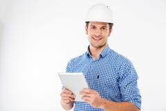 Cheerful man architect in hard hat standing and using tablet Stock Image Cheerful man architect in hard hat standing and using tablet Stock Image