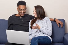 Cheerful mixed race couple use laptop computer for watching movies, sit together on sofa over home interior, browse information, royalty free stock photos Cheerful mixed race couple use laptop computer for watching movies, sit together on sofa over home interior, browse information, royalty free stock photos