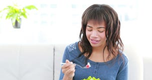 Cheerful pretty woman eating healthy salad sitting on sofa stock video footage Cheerful pretty woman eating healthy salad sitting on sofa stock video footage