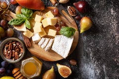 Cheese plate, still life of seasonal wine snacks. Brie cheese, fresh figs, grapes, cheese cubes, pears, pecan nuts and honey on