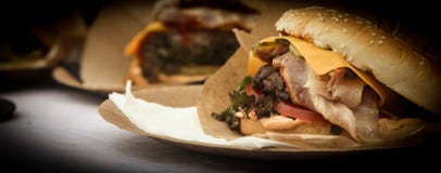 Cheeseburger avec le lard, la viande, les tomates et la salade sur un fond foncé images stock Cheeseburger avec le lard, la viande, les tomates et la salade sur un fond foncé images stock