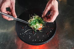Chef, der gesunden Salat auf einem Schwarzblech mit Pinzette beendet fast servierfertig es auf einer Tabelle lizenzfreies stockfoto Chef, der gesunden Salat auf einem Schwarzblech mit Pinzette beendet fast servierfertig es auf einer Tabelle lizenzfreies stockfoto