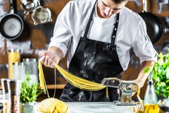 Chef making spaghetti noodles with pasta machine on kitchen table with some ingredients around royalty free stock image Chef making spaghetti noodles with pasta machine on kitchen table with some ingredients around royalty free stock image