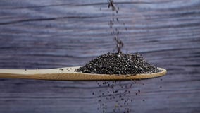 Chia seeds falling into a wooden spoon on gray background