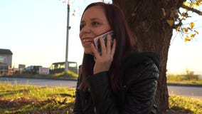 Chica joven que habla en el teléfono en el otoño en el parque en la puesta del sol almacen de video Chica joven que habla en el teléfono en el otoño en el parque en la puesta del sol almacen de video