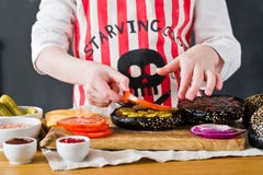 A child in a chef`s apron is preparing a Burger in the kitchen. Recipe for cooking black cheeseberger. Homemade juicy Burger royalty free stock images A child in a chef`s apron is preparing a Burger in the kitchen. Recipe for cooking black cheeseberger. Homemade juicy Burger royalty free stock images