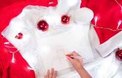 Beautiful creative Christmas background with pattern. The child draws Santa Claus with a red pen on a white sheet and red