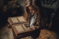 Child girl in image of Sherlock Holmes stands in room and looks photoalbum with magnifier on background of old interior. Closeup. stock images Child girl in image of Sherlock Holmes stands in room and looks photoalbum with magnifier on background of old interior. Closeup. stock images