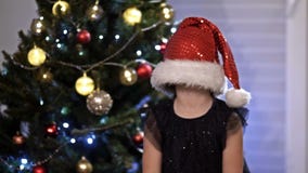 Child girl in Santa hat play hide and seek near a Christmas tree. Playful mood